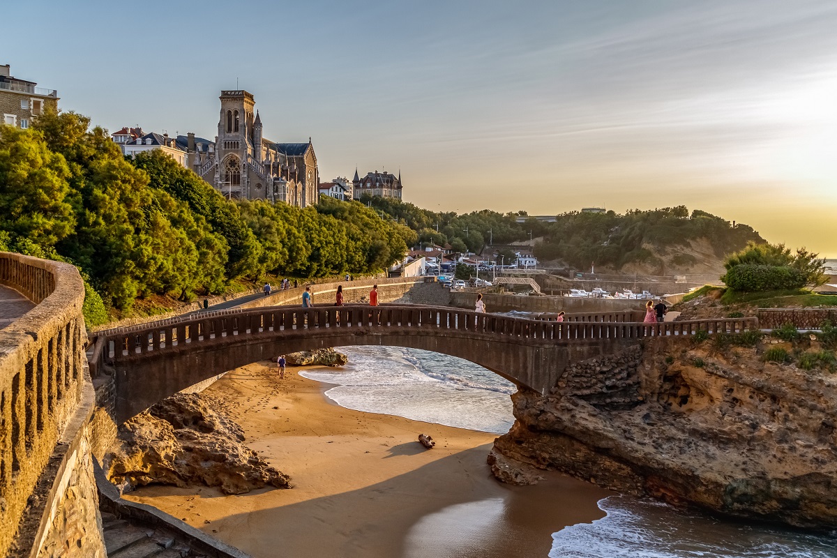 Biarritz, France. View of the famous stone bridge Rocher du Basta, cityscape and coastline with sand beaches and port for small boats. Golden hour. Holidays in France.